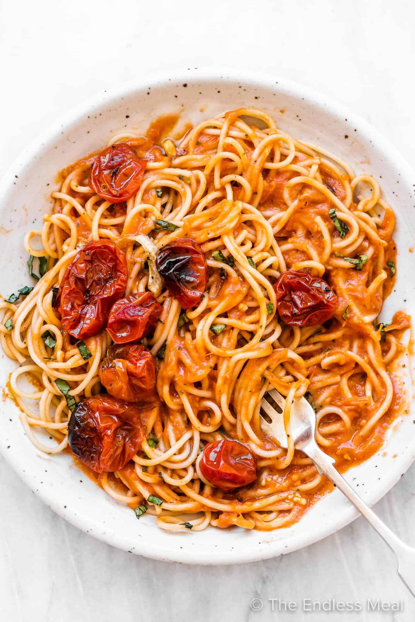 Roasted cherry tomato pasta sauce on spaghetti on a white plate.