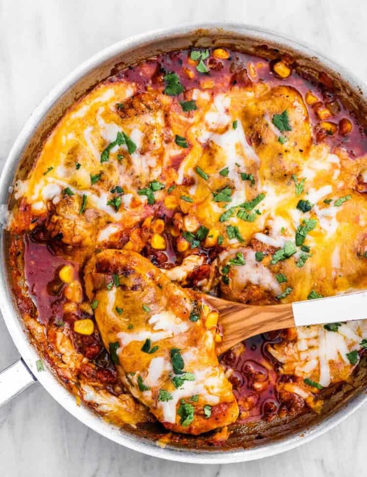 Cheesy salsa chicken in a pan with a wooden spoon.