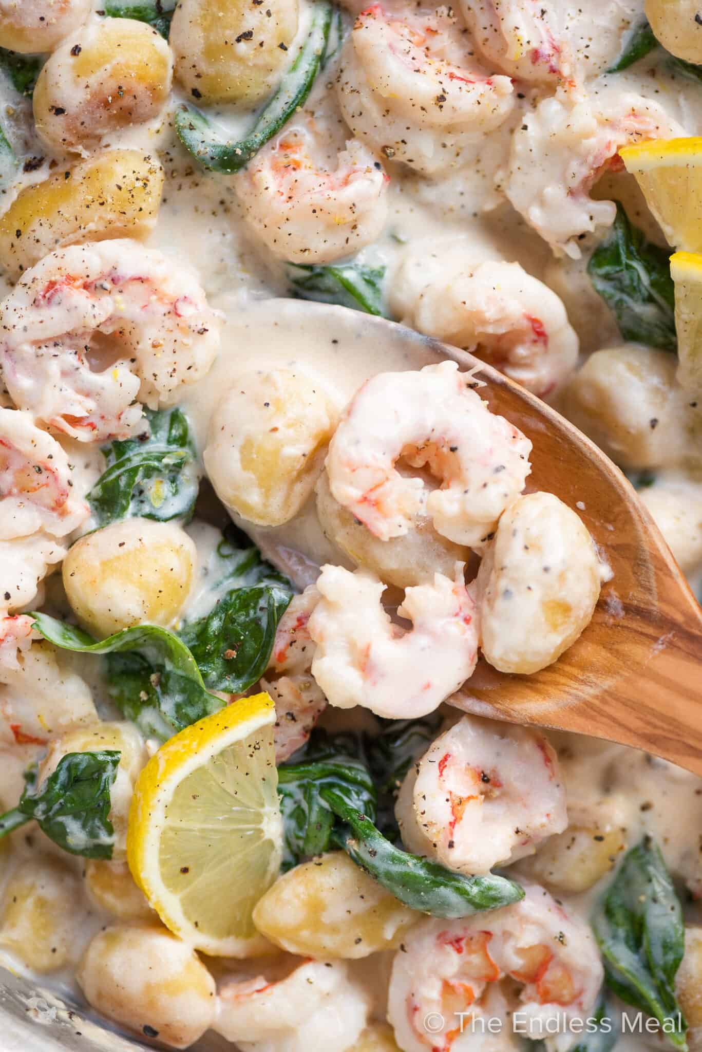 A close up of creamy shrimp gnocchi in a pan with a wooden spoon.