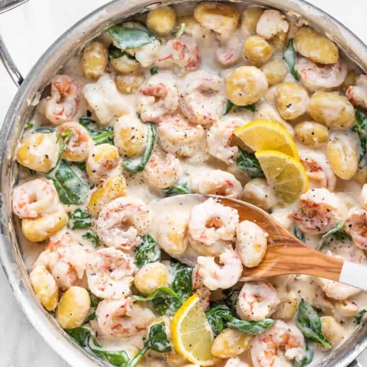 Shrimp and gnocchi in pan with a wooden spoon.