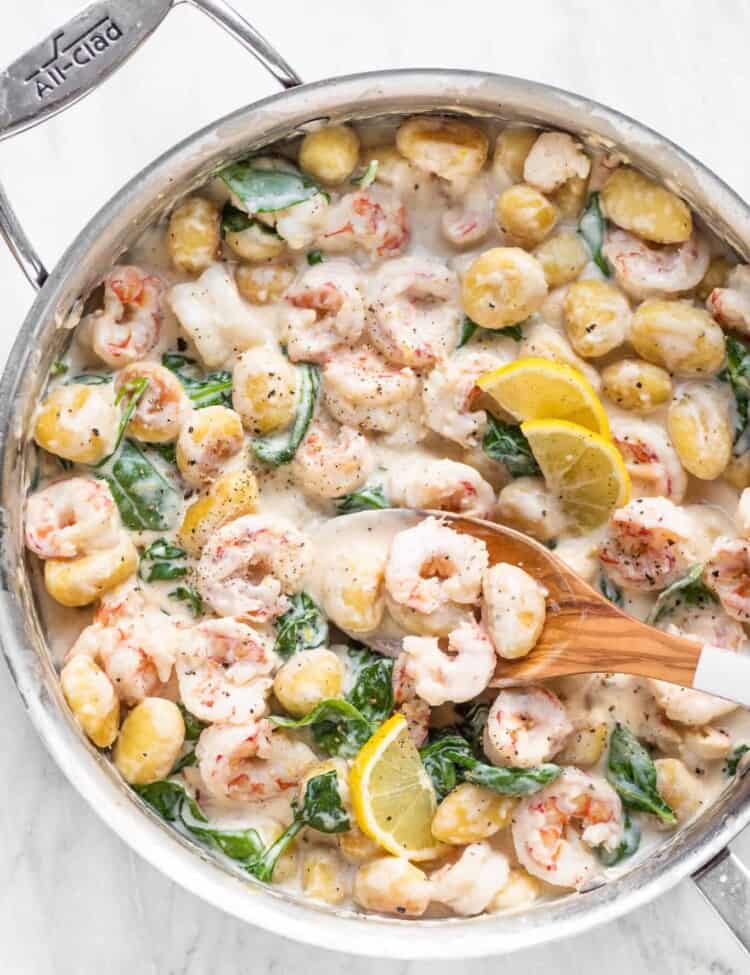 Shrimp and gnocchi in pan with a wooden spoon.