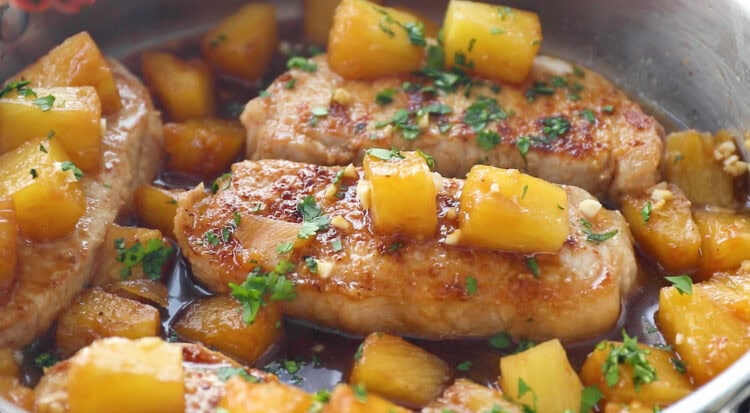 Seared pineapple pork chops topped with juicy pineapple chunks and fresh chopped herbs in a pan with a rich brown sauce.