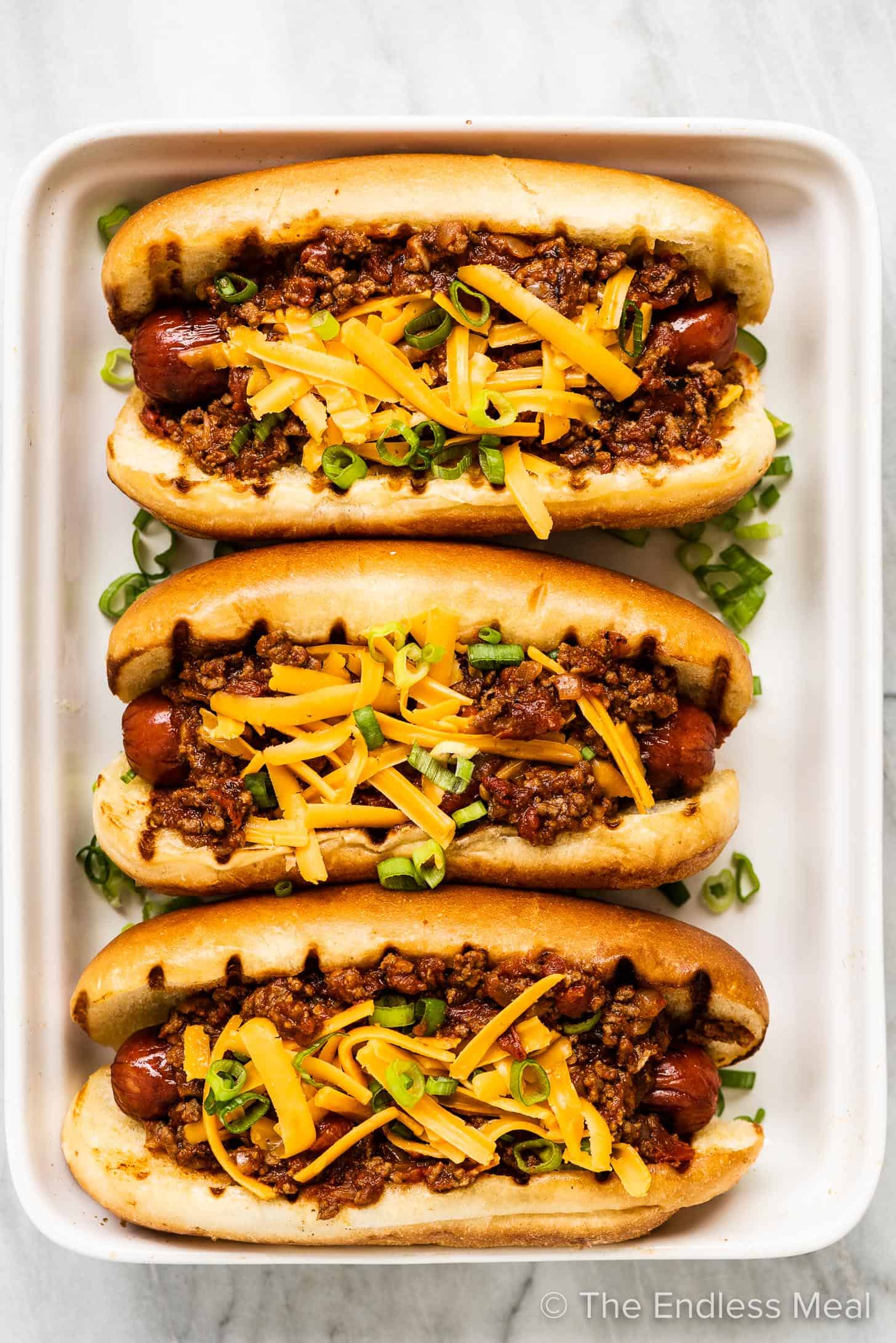 Three chili dogs on a white plate.