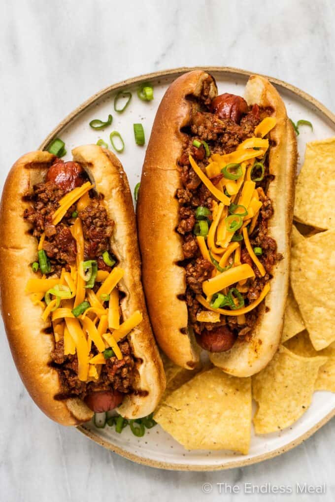 Two chili dogs on a plate with chips.