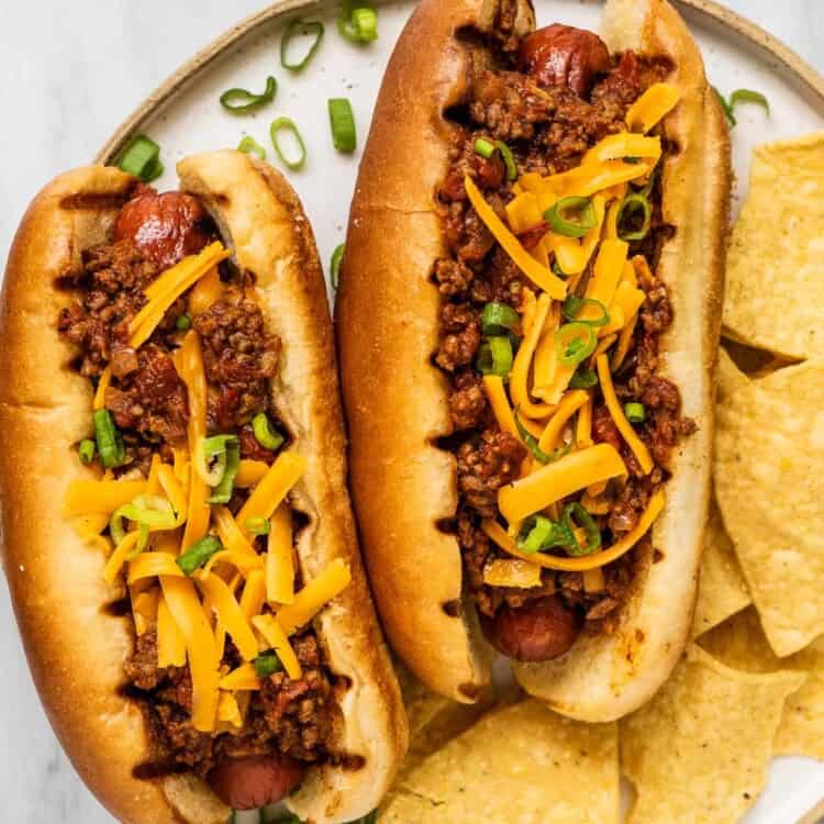 Two chili dogs on a plate with chips.