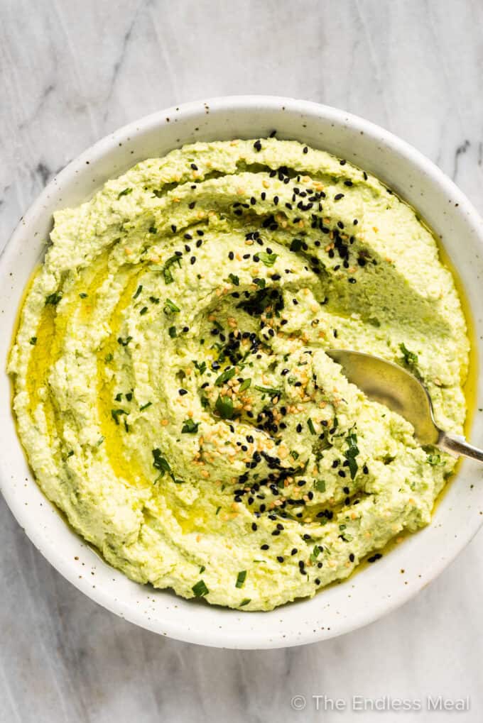 Edamame Hummus in a white bowl with a spoon in it.