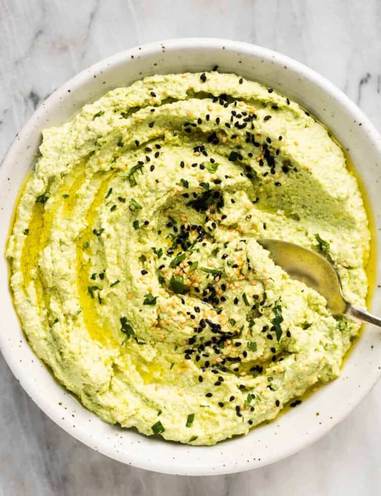 Edamame Hummus in a white bowl with a spoon in it.