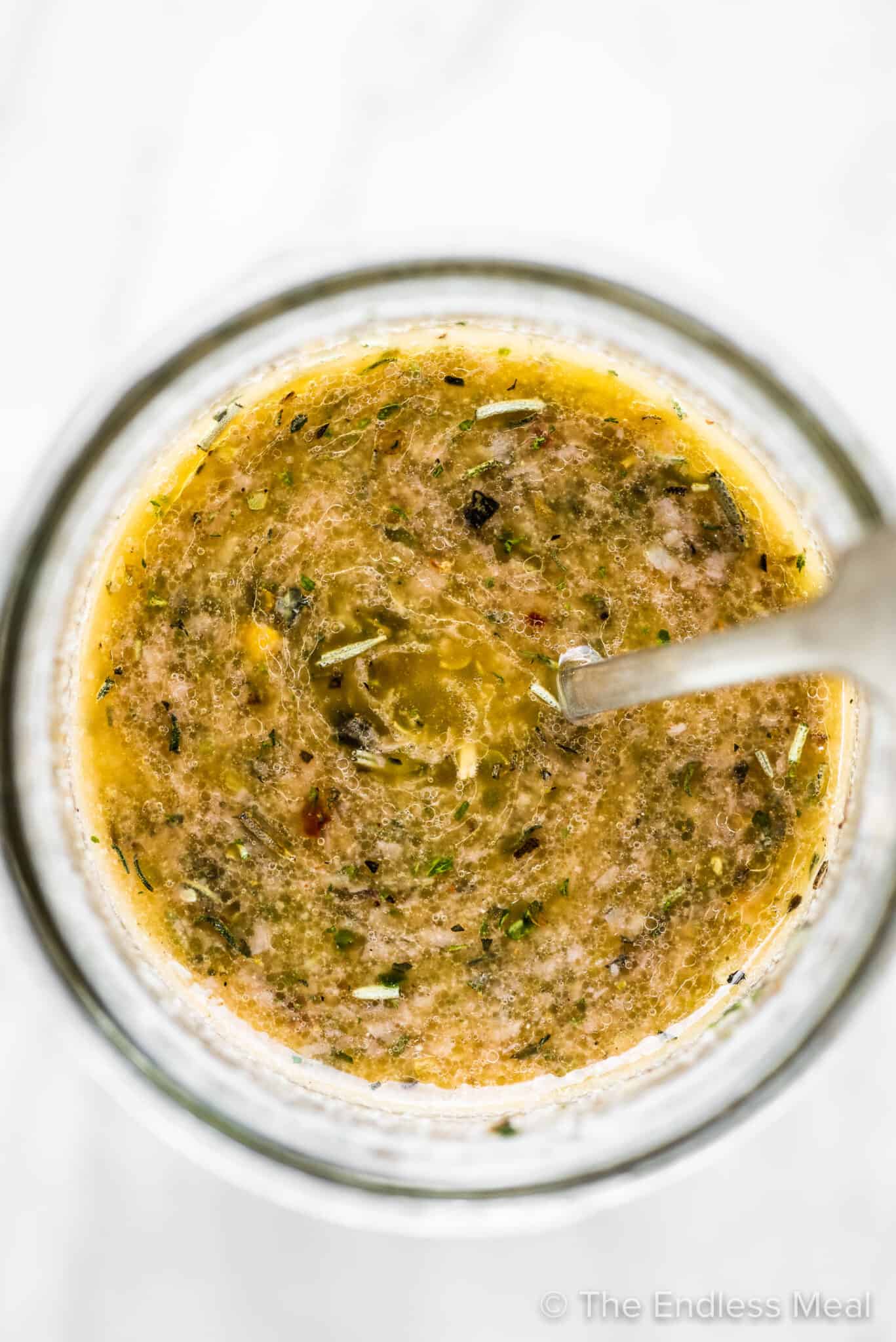 A spoon in a glass jar of Italian salad dressing.