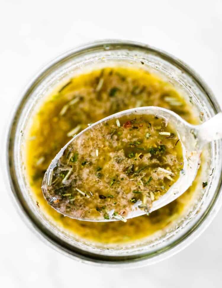 A spoon scooping some homemade italian dressing out of a jar.