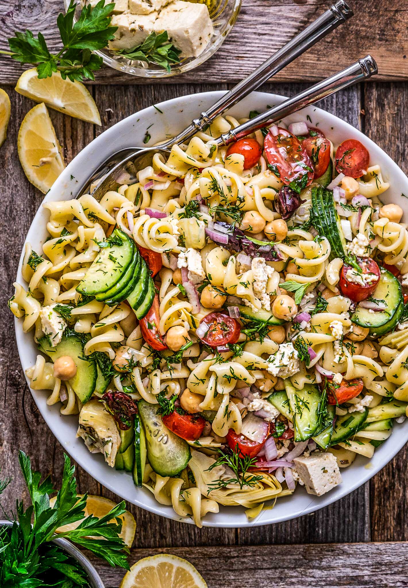 Greek pasta salad in a white bowl with tongs.