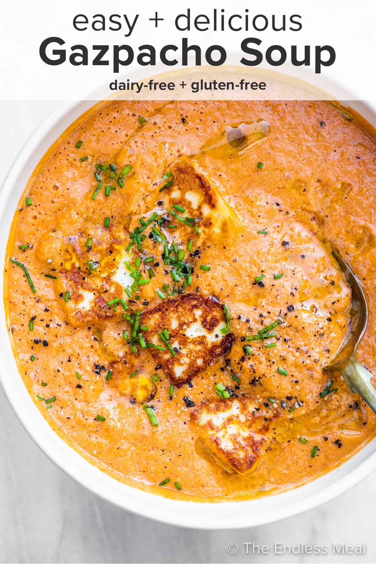 Gazpacho soup in a white bowl with fried halloumi and the recipe title on top of the picture.
