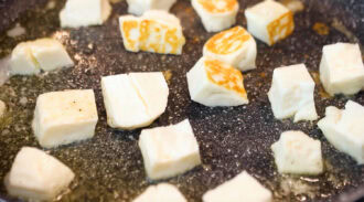 Cubes of white cheese are frying in a pan, with some pieces browned on one side and others still white.