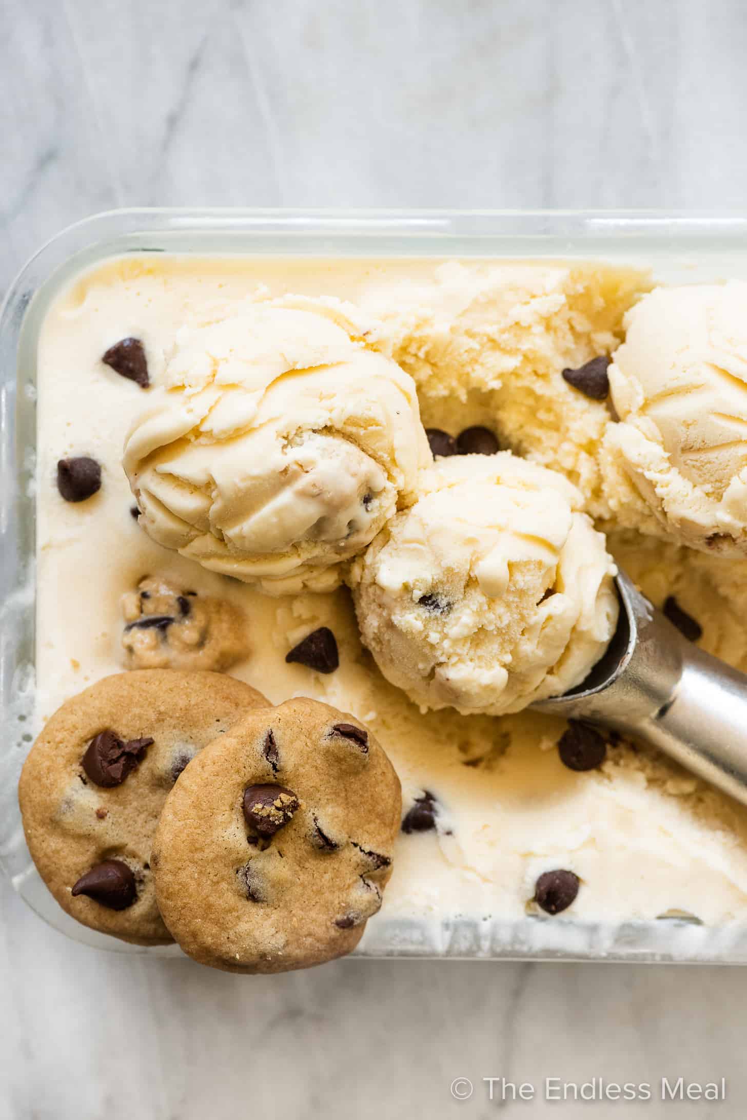 Chocolate Chip Cookie Dough Ice Cream in a glass container with an ice cream scoop and cookies. 