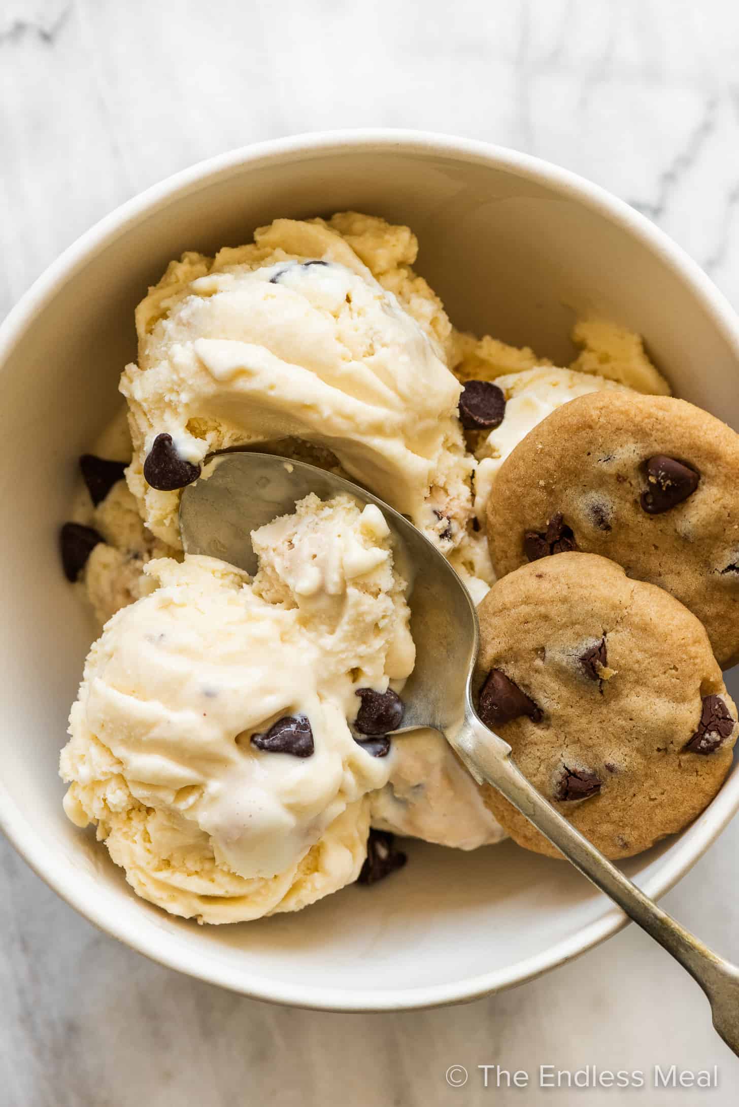 Chocolate Chip Cookie Dough Ice Cream in a white bowl with a spoon and 2 cookies. 