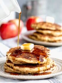 a stack of pancakes with maple syrup being poured over them