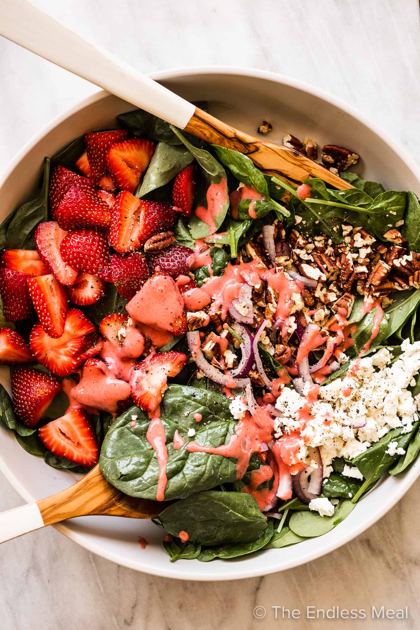 strawberry spinach salad dressing poured over a serving bowl of strawberry spinach salad. 