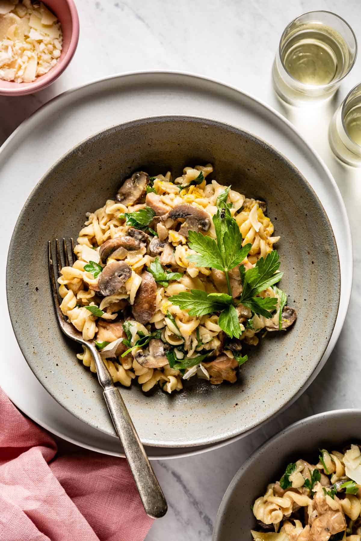 A bowl of this chicken and mushroom recipe garnished with parsley with a fork in the dish.