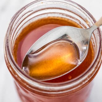 A spoon scooping hot honey out of a glass jar.