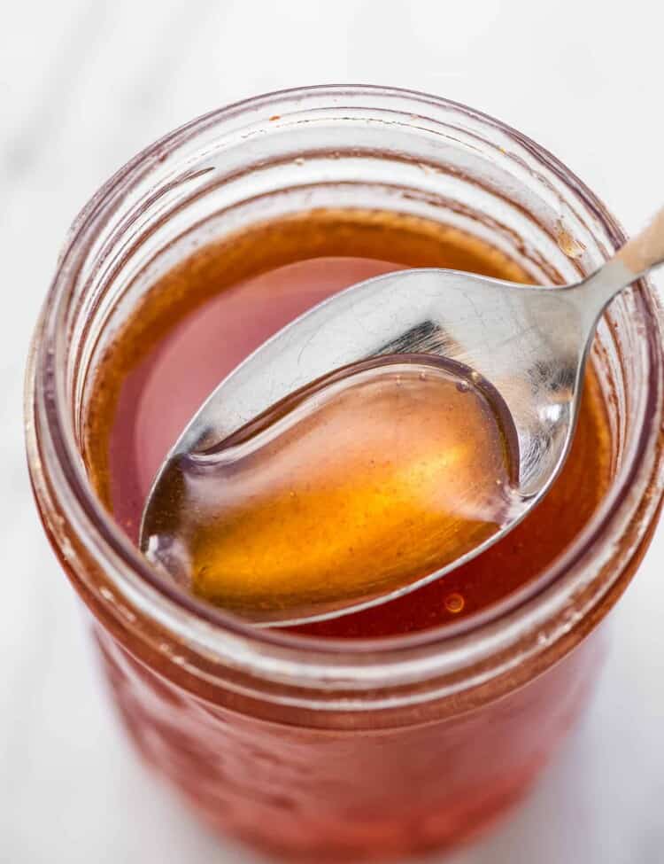 A spoon scooping hot honey out of a glass jar.