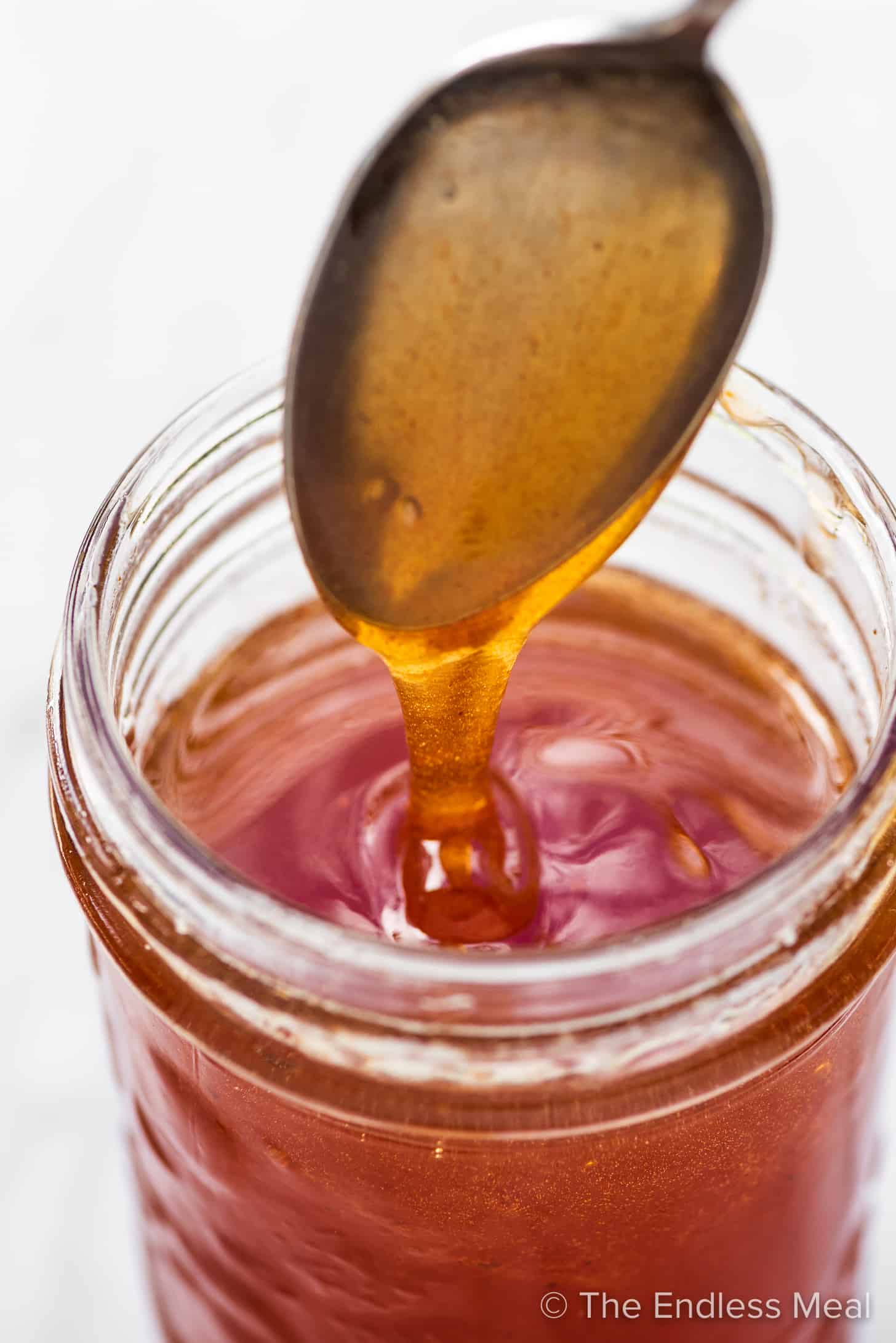 A spoon drizzling hot honey from a jar.