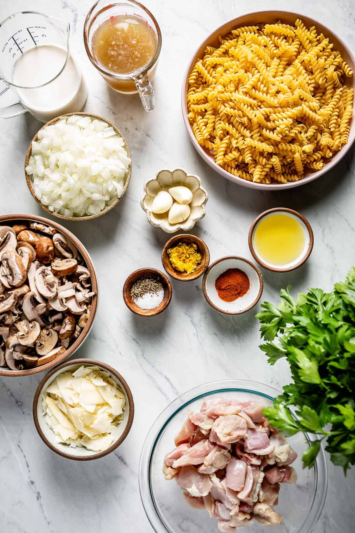 Ingredients for this chicken and mushroom pasta recipe are portioned and laid out on a marble backdrop