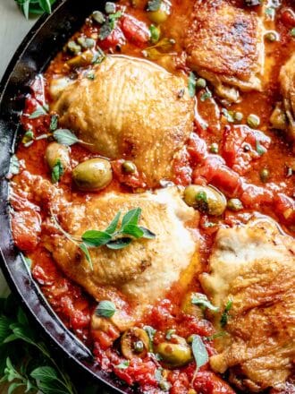 close up of a skillet with tomato sauce, olives, capers and crispy chicken thighs