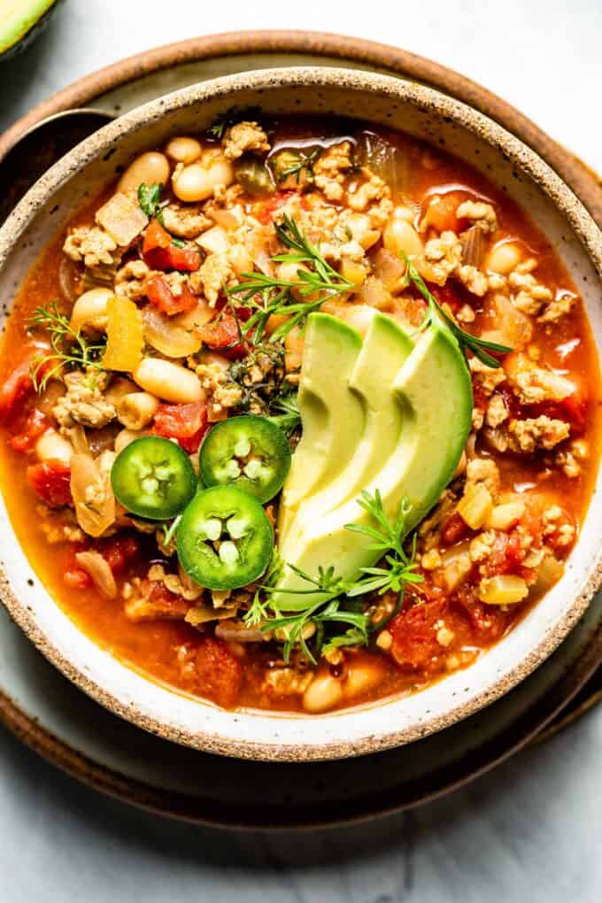 A bowl of buffalo chicken chili with avocado on top.