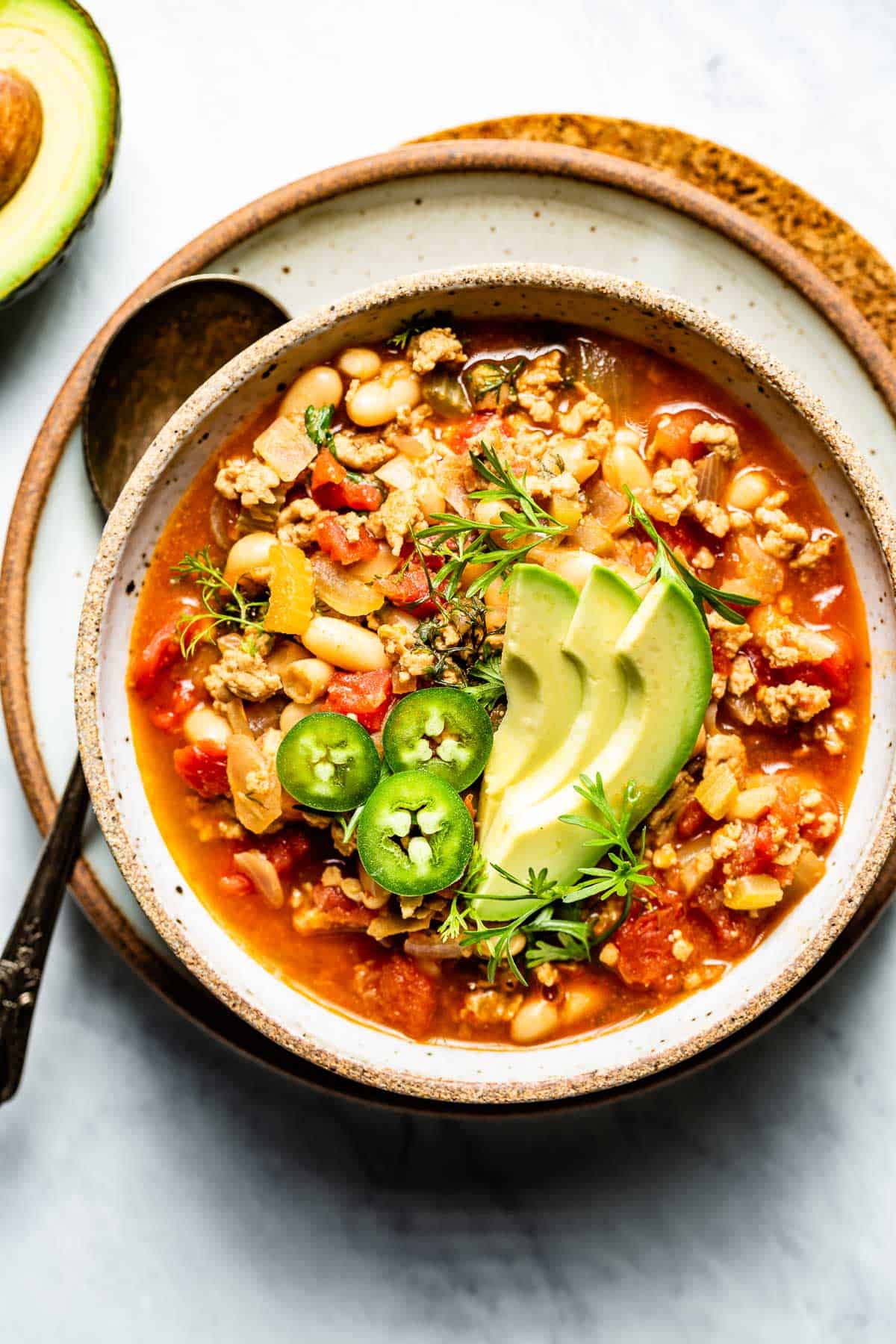 White bean buffalo sauce chili in a bowl garnished with jalapenos and avocado slices.