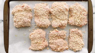 Eight pieces of breaded raw chicken are arranged on a baking sheet lined with parchment paper, ready to be cooked.