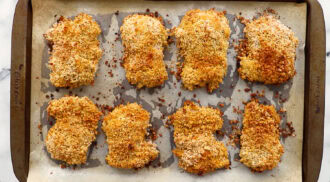 Eight breaded and baked chicken cutlets arranged on a parchment-lined baking sheet, viewed from above.