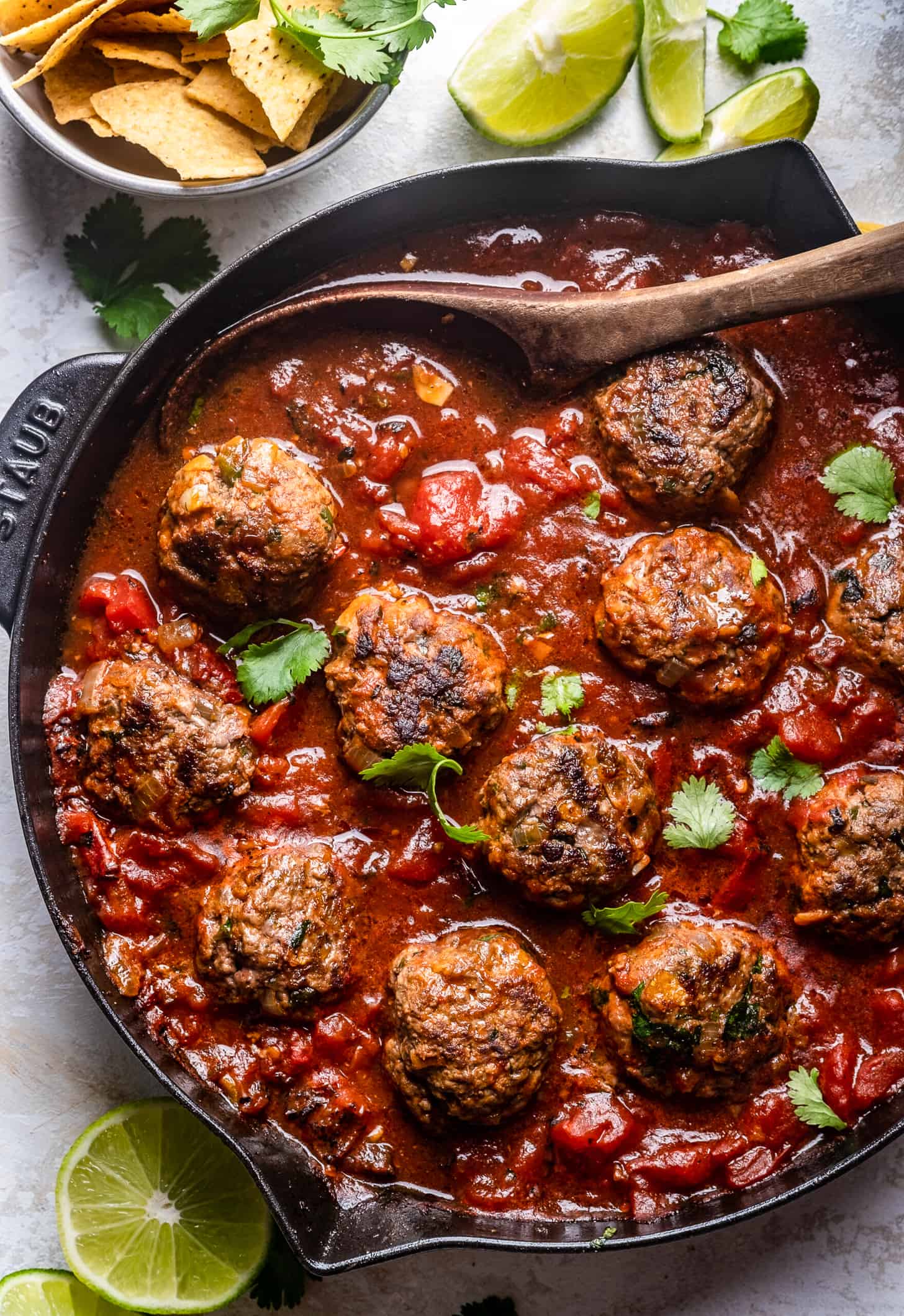 Tex-Mex Meatballs in a skillet in tomato sauce with a wooden spoon.
