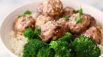 Bowl of white rice topped with glazed meatballs, sprinkled with sesame seeds and green onions, served with steamed broccoli.
