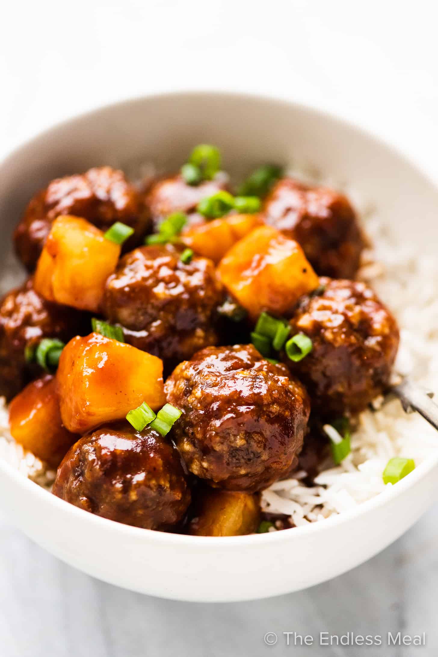 side angle of Hawaiian pineapple meatballs in a bowl with rice.