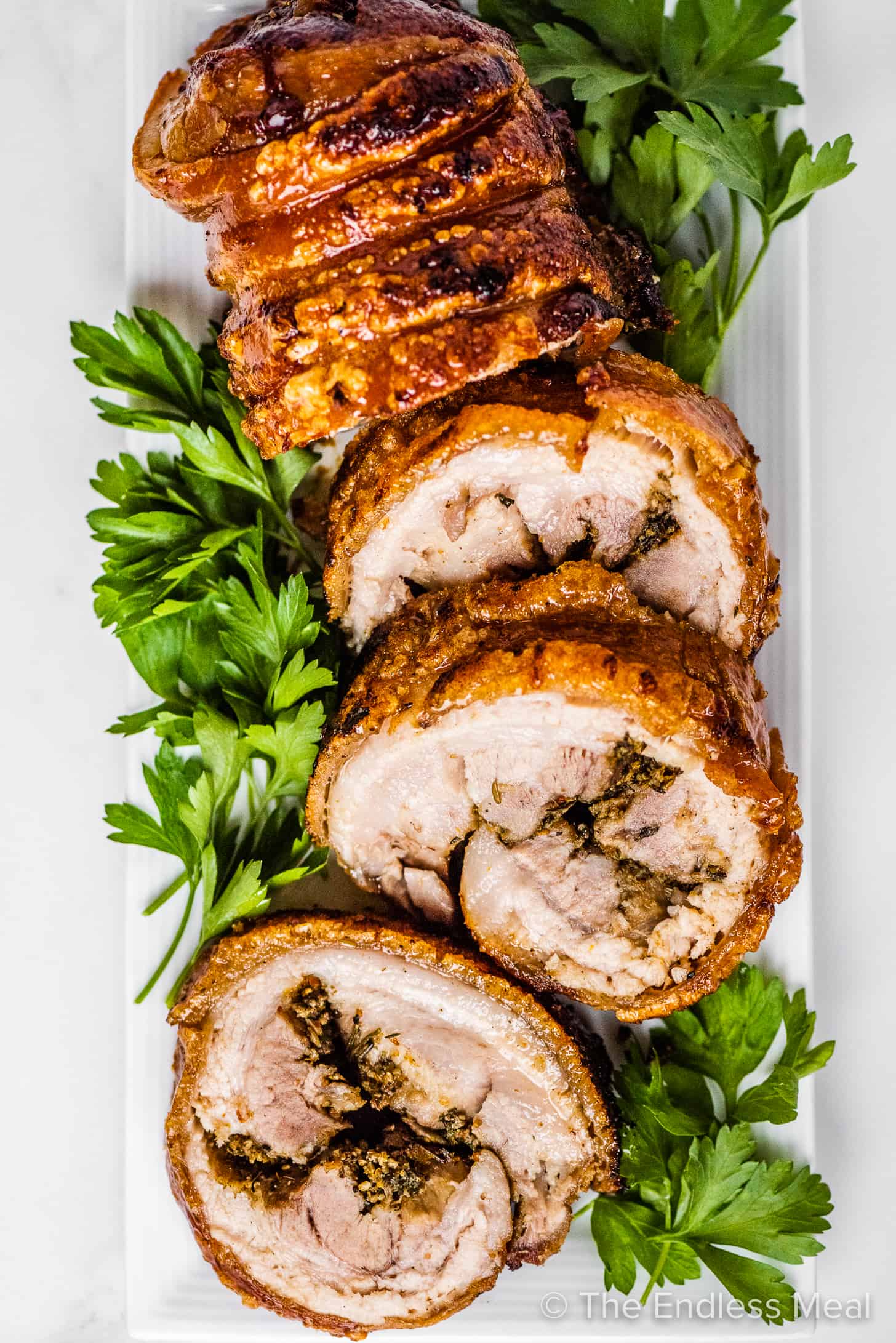 Porchetta sliced into rounds on a serving tray with Italian parsley.