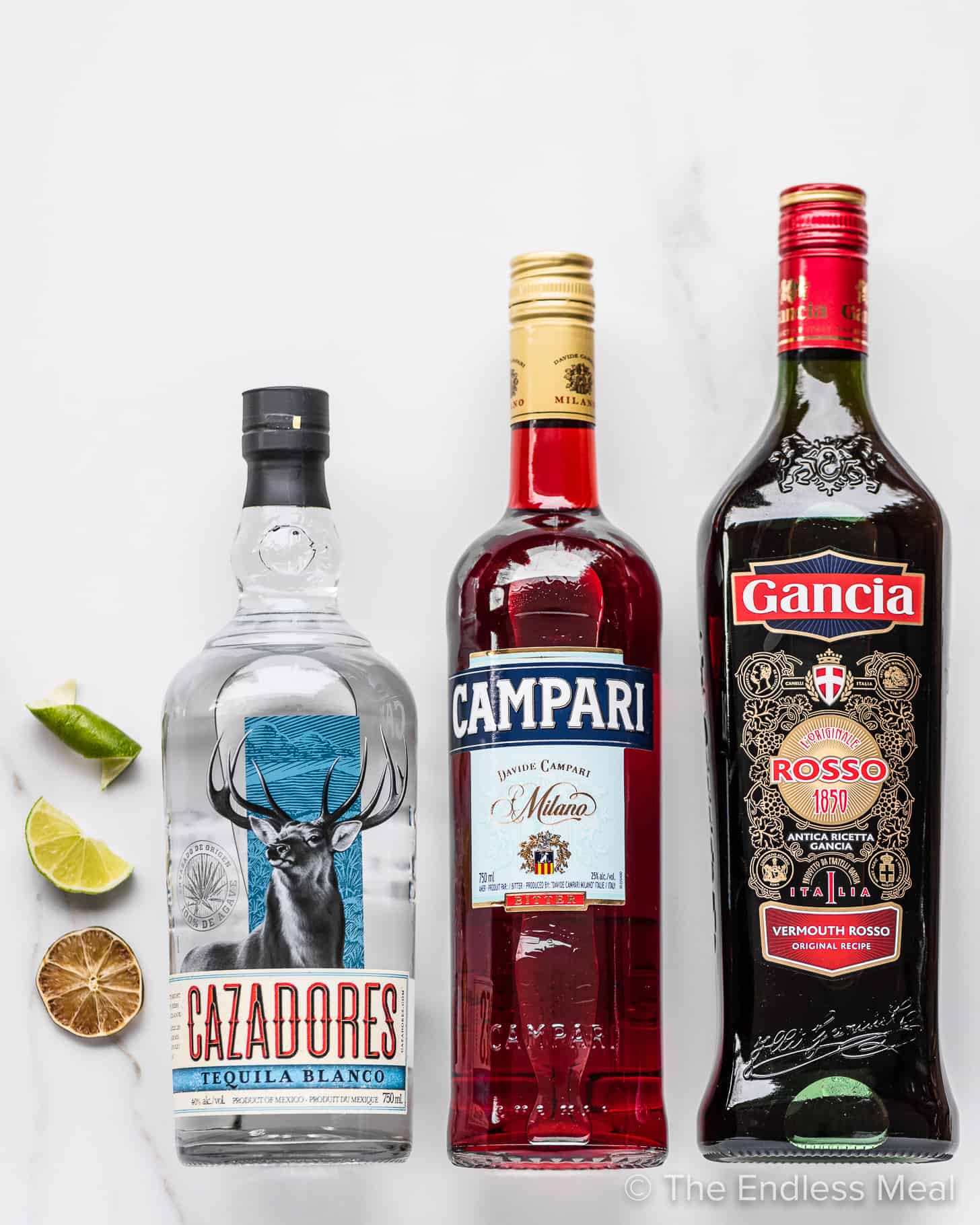 The ingredients to make a Tequila Negroni on a marble countertop.