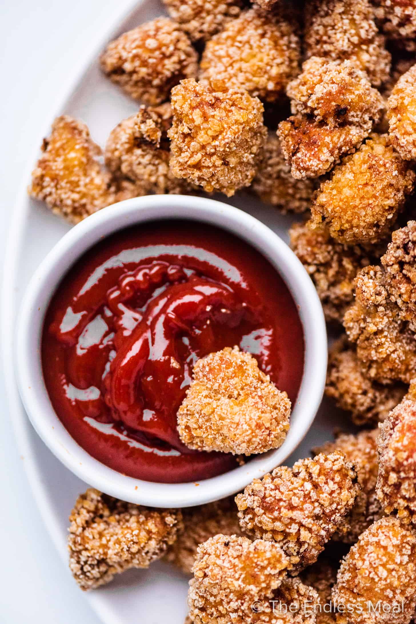 A crispy fried chicken bite being dipped into ketchup.