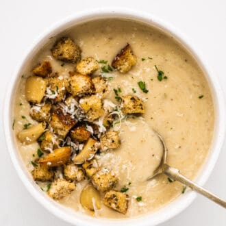 a bowl of garlic soup topped with croutons and roasted garlic.