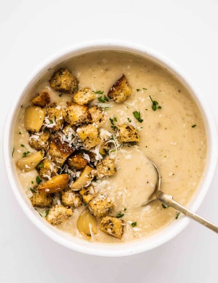 a bowl of garlic soup topped with croutons and roasted garlic.