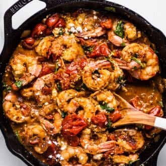 Greek Shrimp with Tomatoes and Feta in a cast iron pan with a wooden spoon.