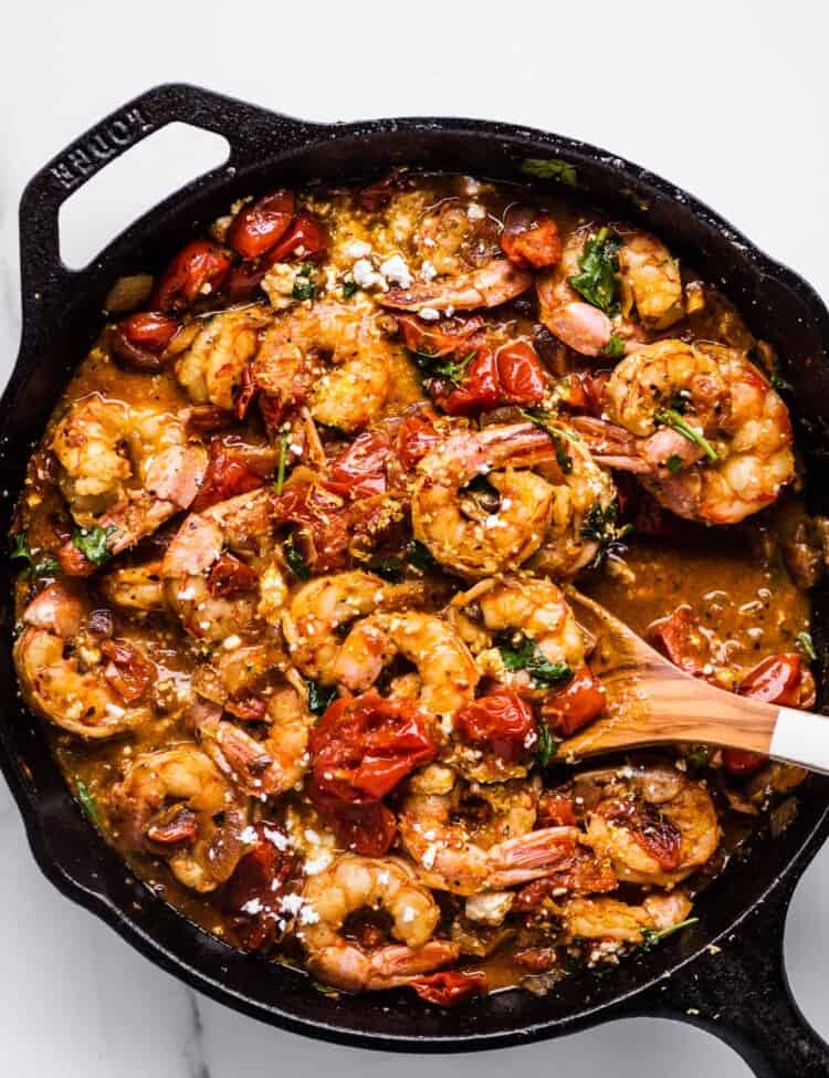 Greek Shrimp with Tomatoes and Feta in a cast iron pan with a wooden spoon.