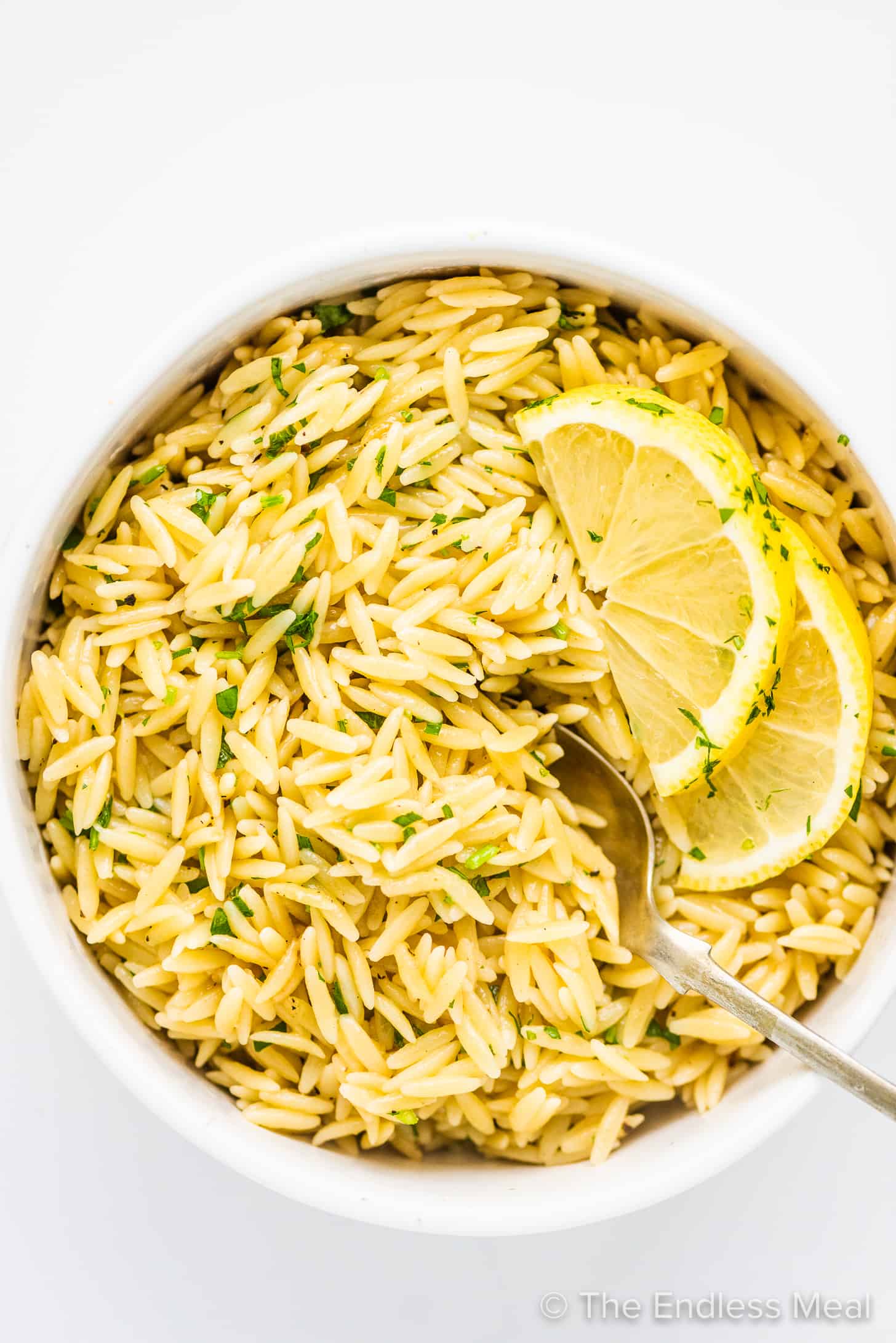 Lemon butter orzo in a white bowl with a serving spoon,