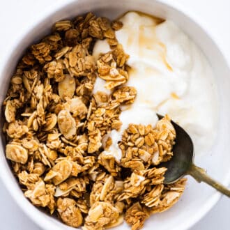 Vanilla Almond Granola with yogurt and maple syrup in a white bowl.