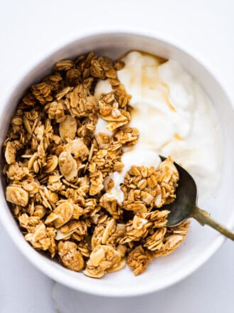Vanilla Almond Granola with yogurt and maple syrup in a white bowl.