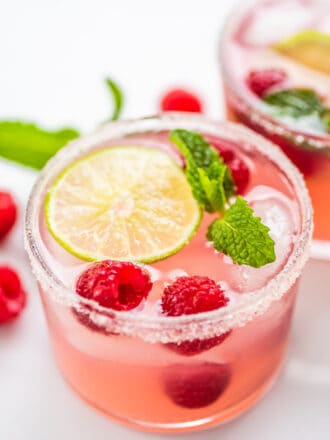 2 glasses of Pink Lemonade Margarita garnished with raspberries and mint.