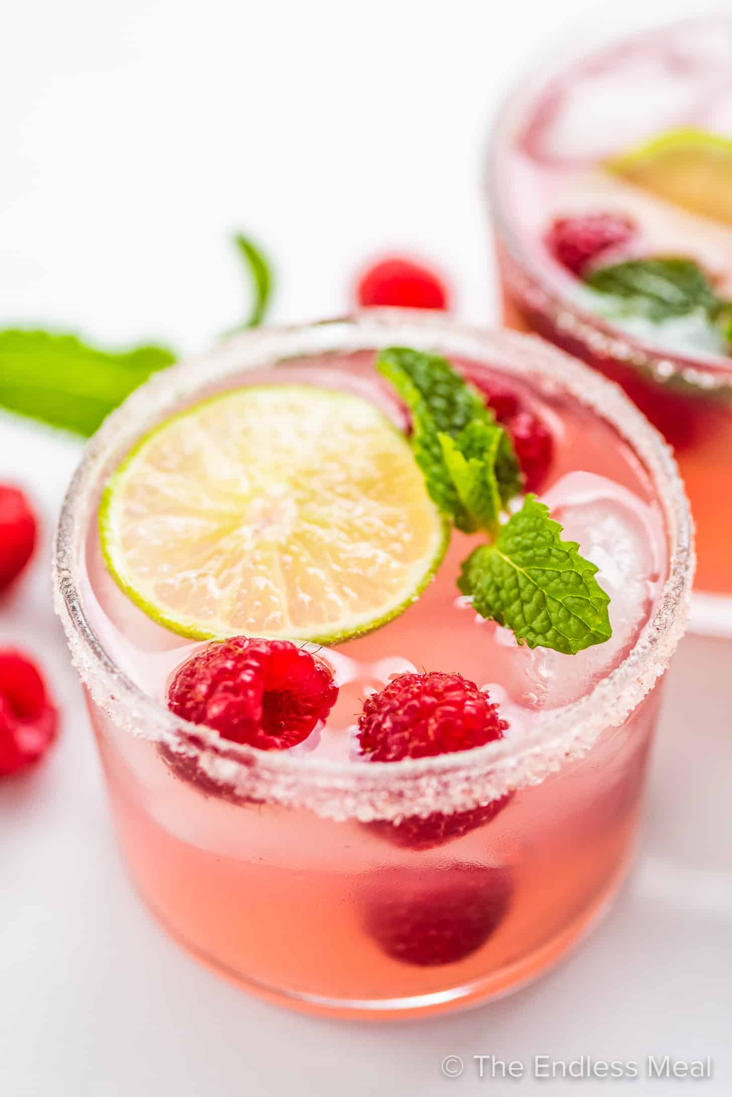 2 glasses of Pink Lemonade Margarita garnished with raspberries and mint.
