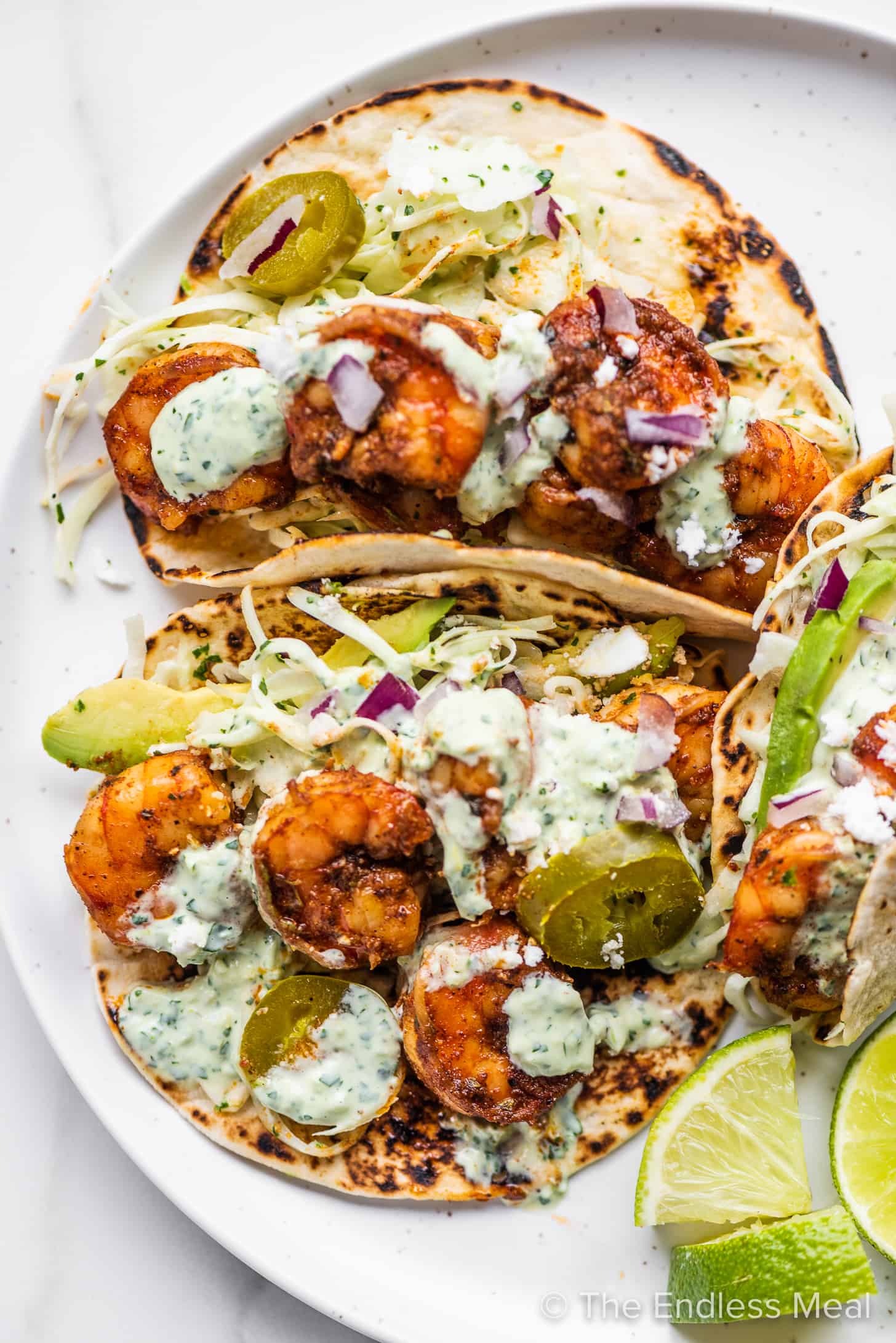 three shrimp tacos with slaw on a plate with limes