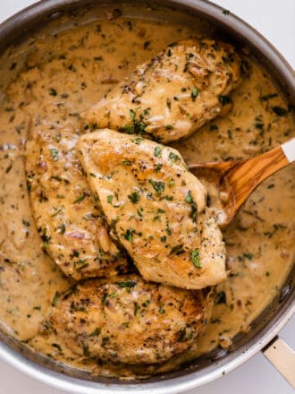 creamy tarragon chicken in a pan with a wooden spoon.