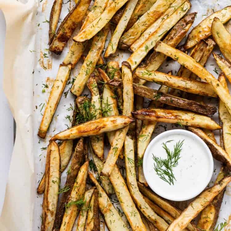 dill french fries on a baking sheet with dill yogurt dip