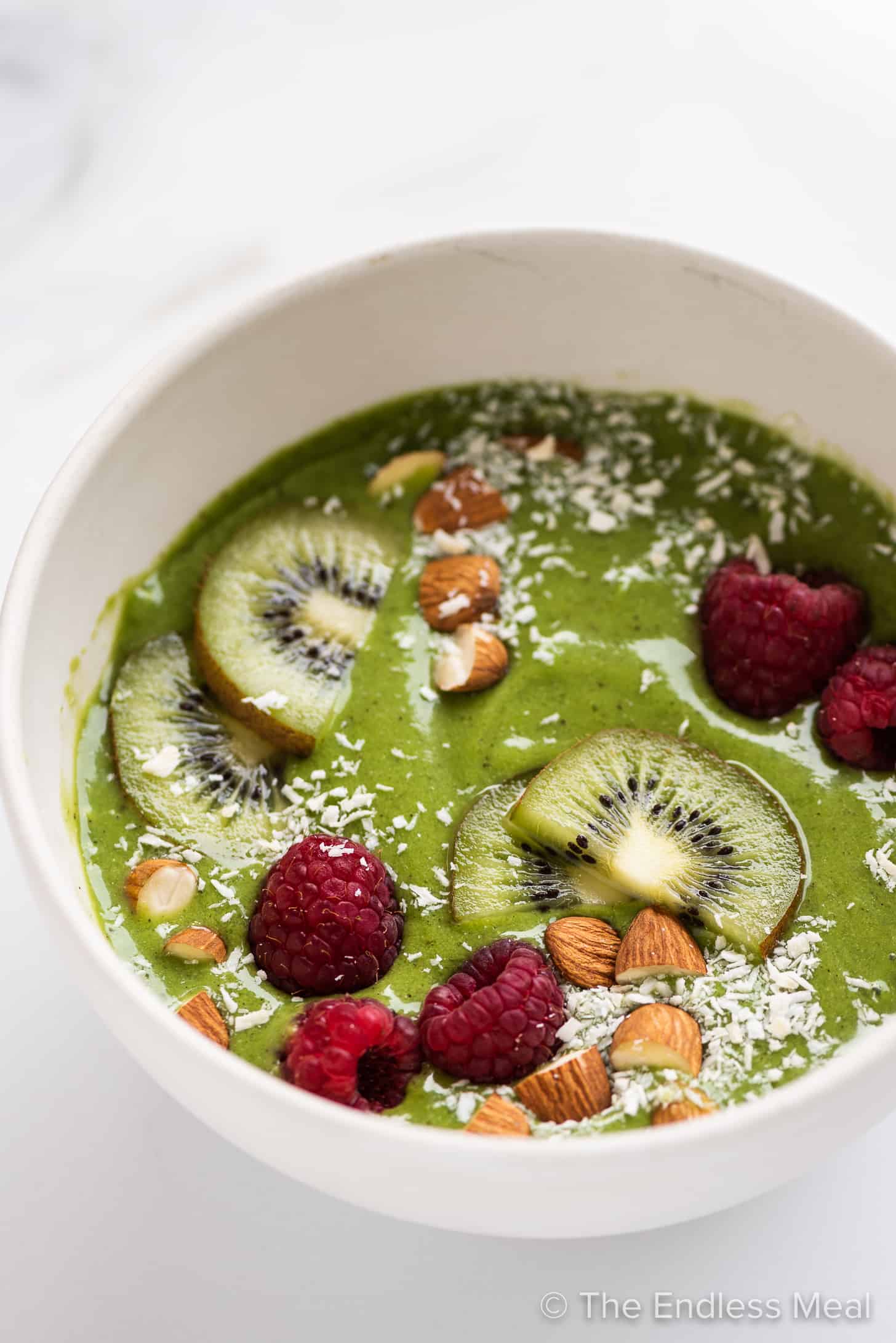 a green smoothie in a bowl with fruit and nuts.
