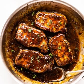 a spoon pouring honey mustard sauce over pork chops in a pan